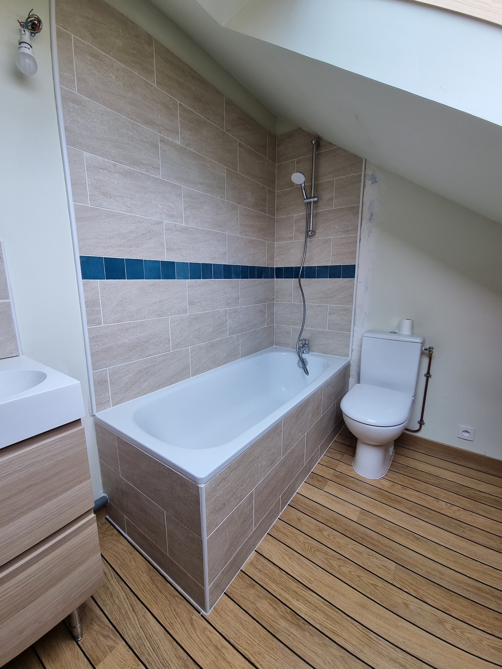 Aménagement d'une salle d'eau sous pente avec baignoire et parquet.