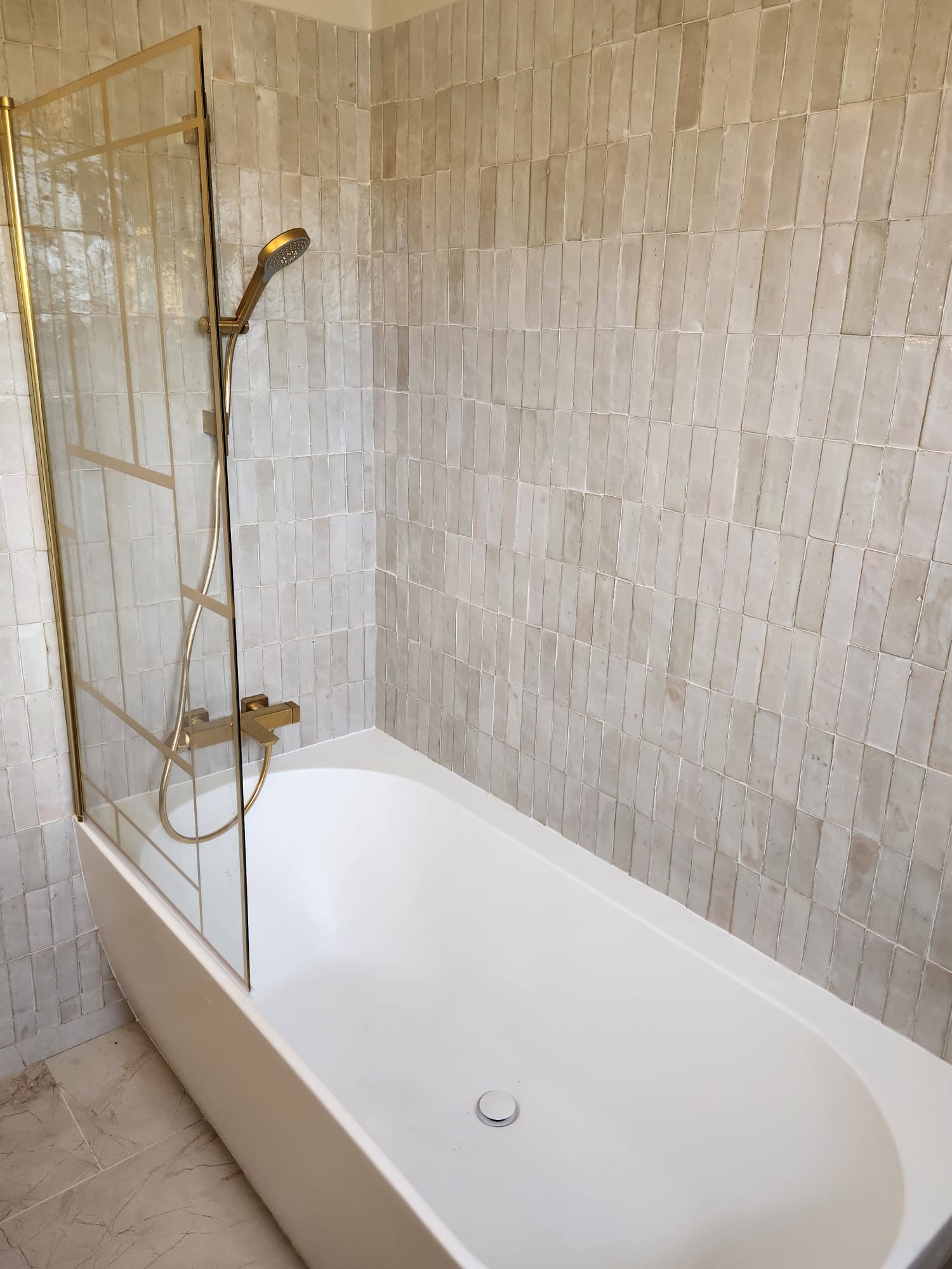 Détail d'une baignoire avec paroi vitrée et robinetterie dorée.