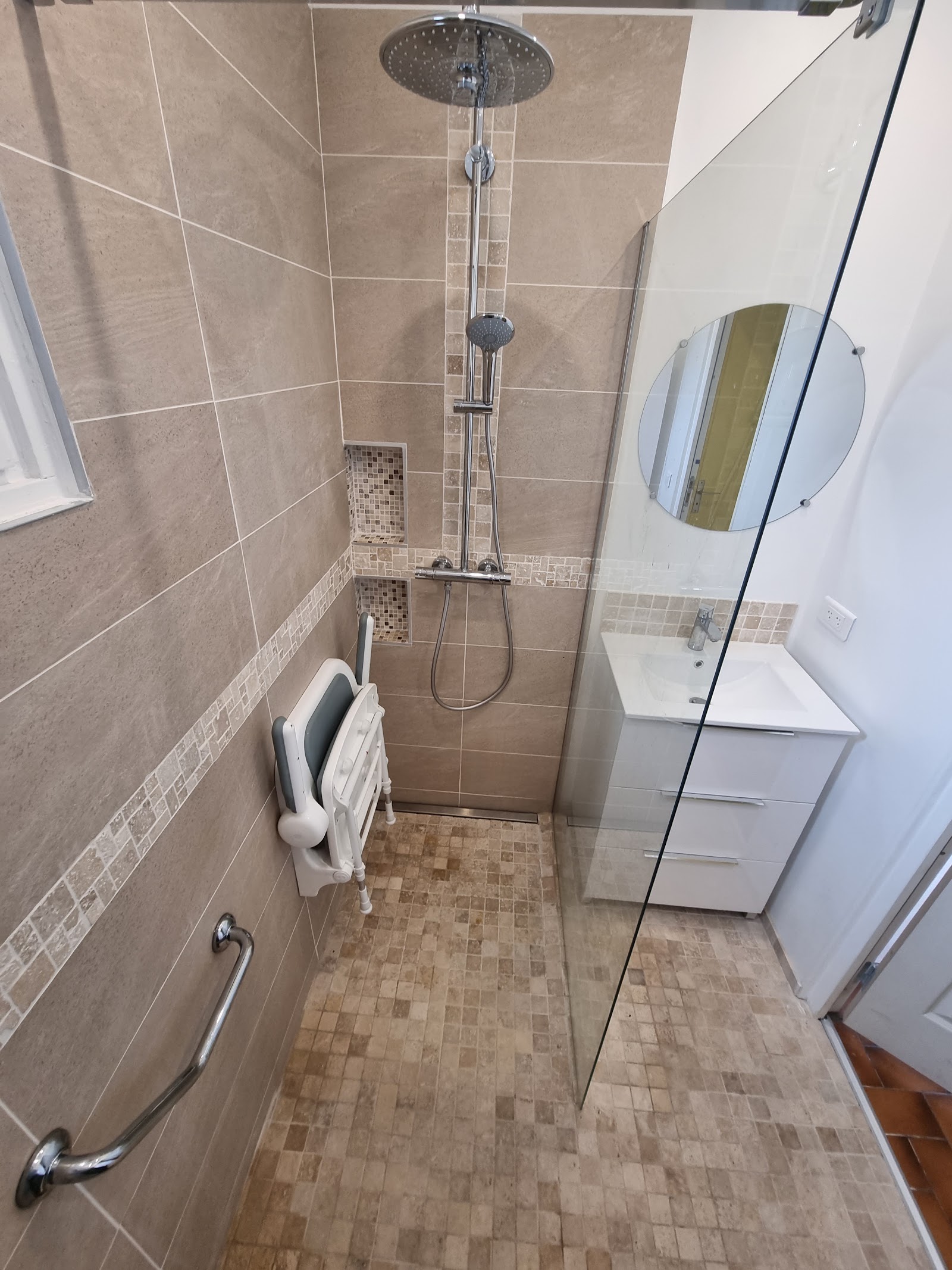 Douche à l'italienne PMR avec siège rabattable et barre de maintien.